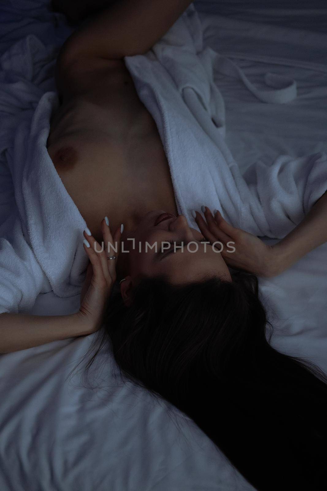 From above of topless sexy female in bathrobe lying on comfortable bed in bedroom