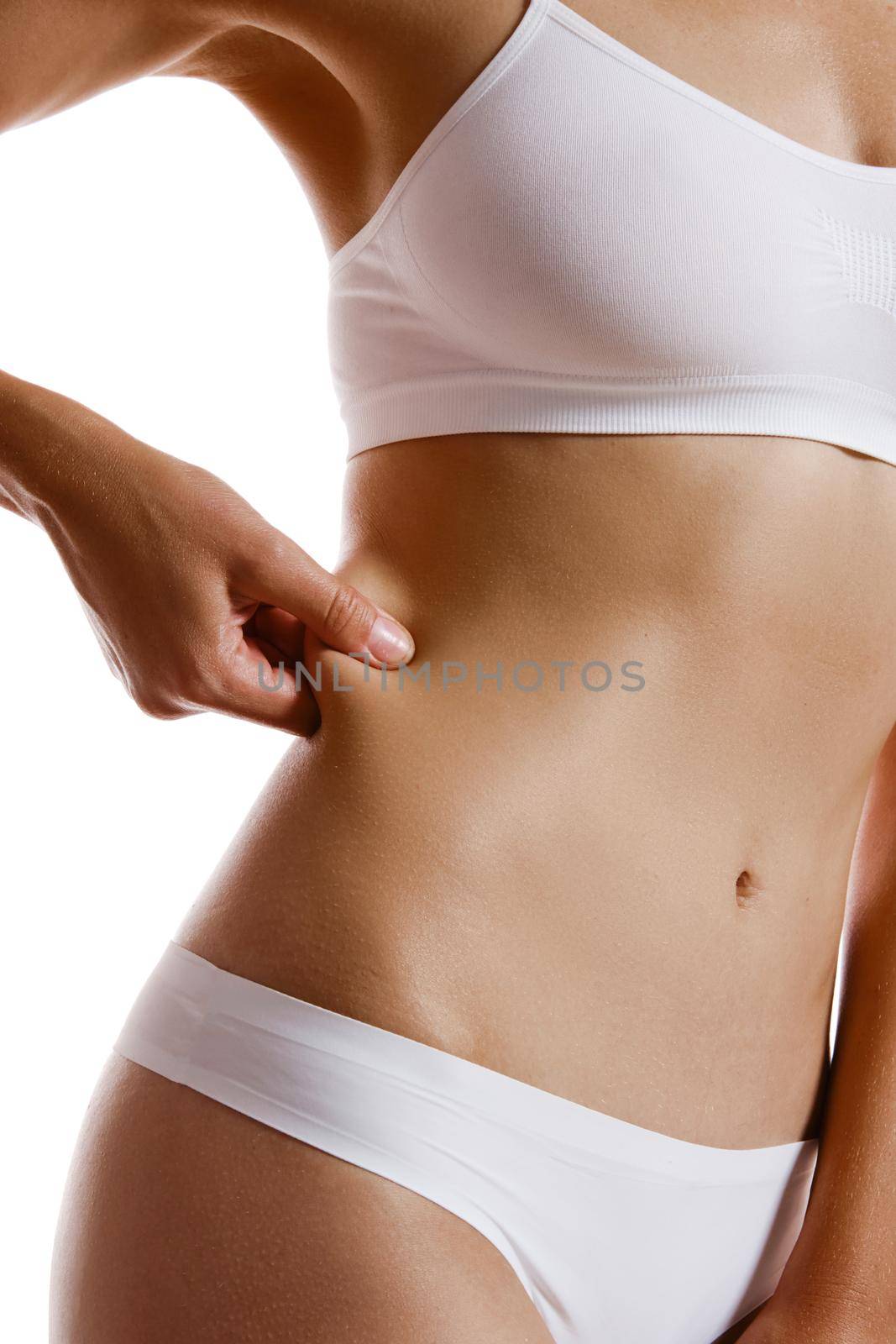 Perfect, slim, toned, young body of a sexy girl in white underwear. She is showing fat on her side while posing sideways isolated on white. Beauty treatment. Plastic surgery and aesthetic cosmetology concept. Augmentation or reduce of a breast, cellulite removal. High resolution, close-up shot.