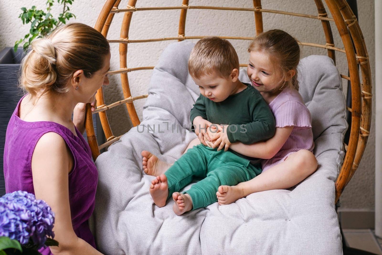 Mother son and daughter are sitting on the balcony with flowers and laughing