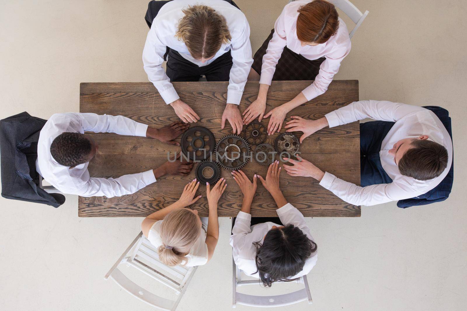 Group of business people joining together metal gears on table at workplace top view