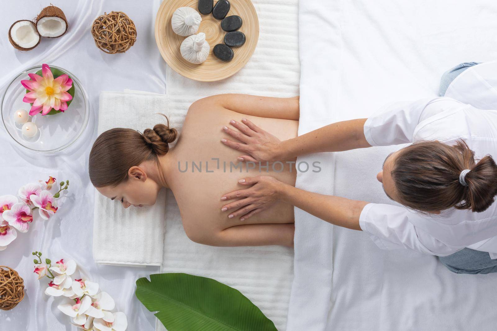 Woman at spa thai massage tow view, beauty treatments concept. Orchid and lotus flowers coconut stones and herb pouches