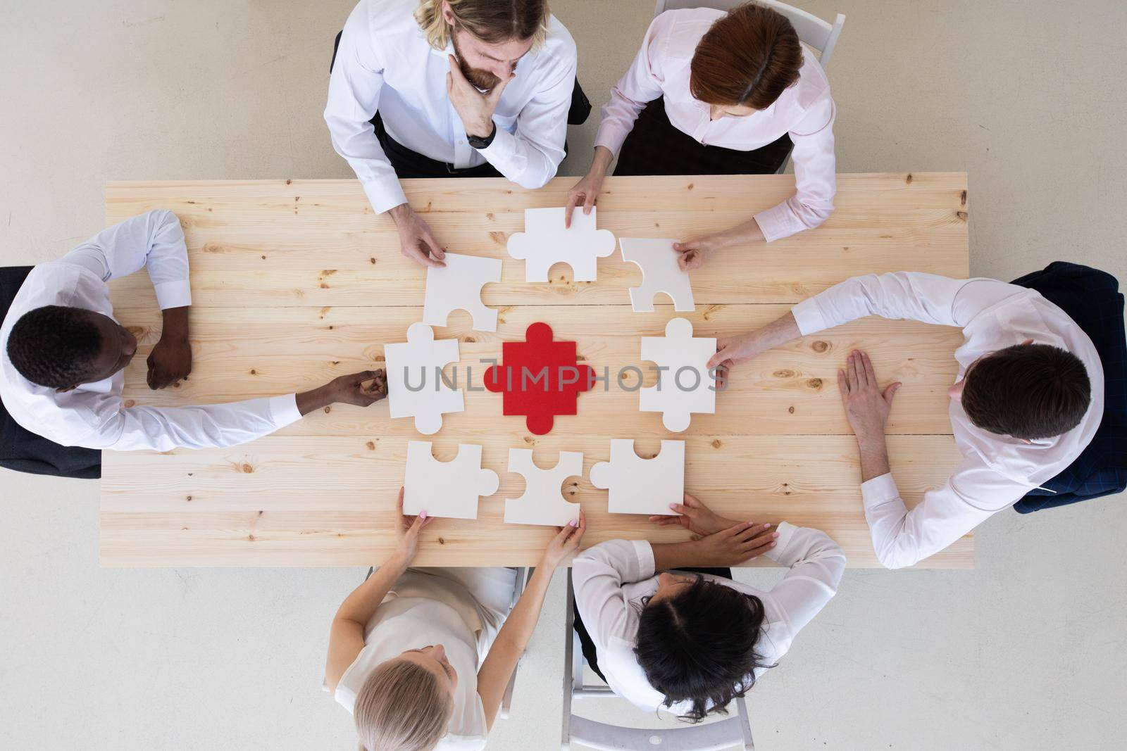 Diverse business people helping in assembling puzzle, cooperation in decision making, team support in solving problems and corporate group teamwork concept, connecting pieces