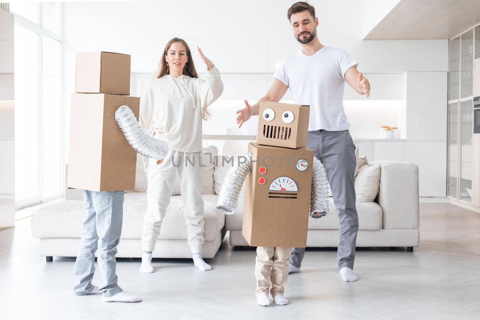 Happy family of parents and two children playing dancing like robots at home, children wearing handmade moving box costume of cardboard