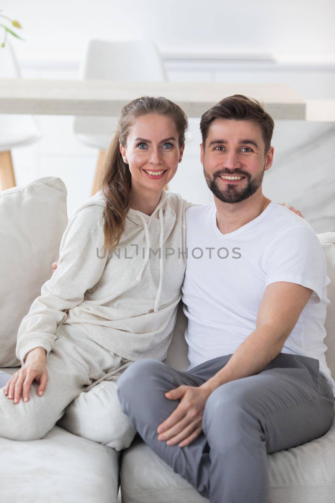 Portrait of smiling young man and woman spouse renters sit relax on comfortable couch in new apartment or house. Happy Caucasian couple rest on sofa in living room, moving to own home. Rental concept.