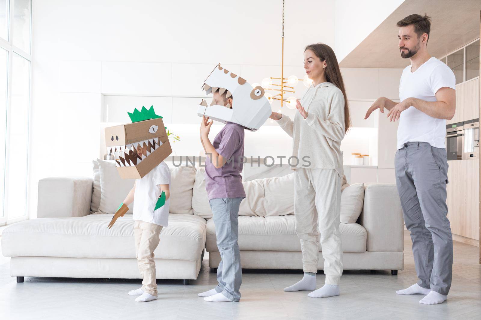 Happy family of parents and two children playing dinosaurs at home, children wearing handmade costume mask of cardboard