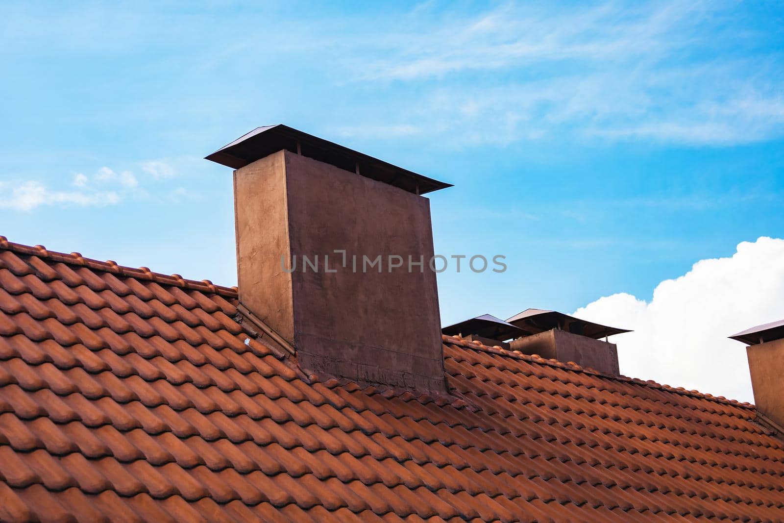 Red roof tiles with red chimney on blue sky background. Old and used overlapping red classic style roofing material. Spanish tiled roof. Mediterranean architecture