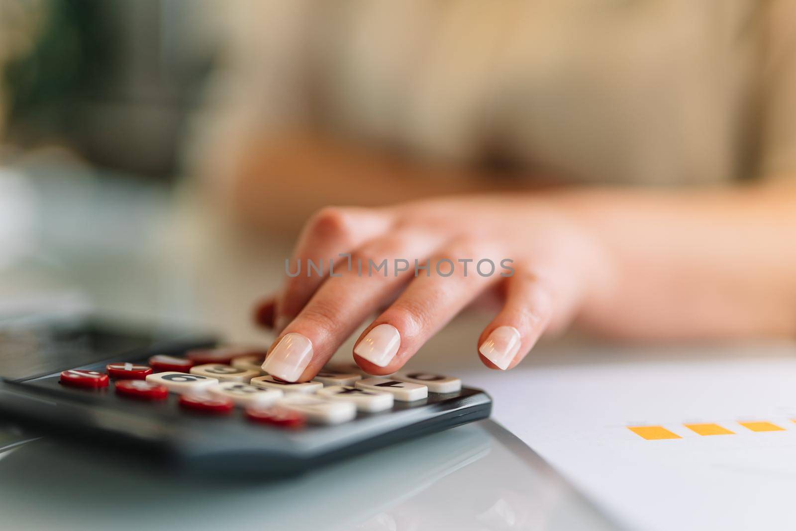 Close-up of a young woman's hand typing on her calculator as she works. Doing financial mathematical operations on a calculator. Young businesswoman and entrepreneur working in office or at home in white shirt.