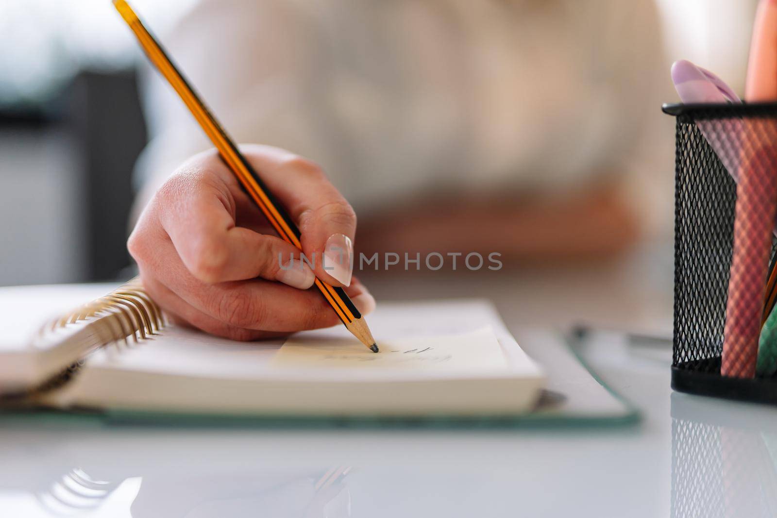 Close-up of the hand of a young girl in a white shirt writing with a pencil in her diary or notebook. Young entrepreneur and businesswoman teleworking. Young girl taking notes while studying. Woman studying.