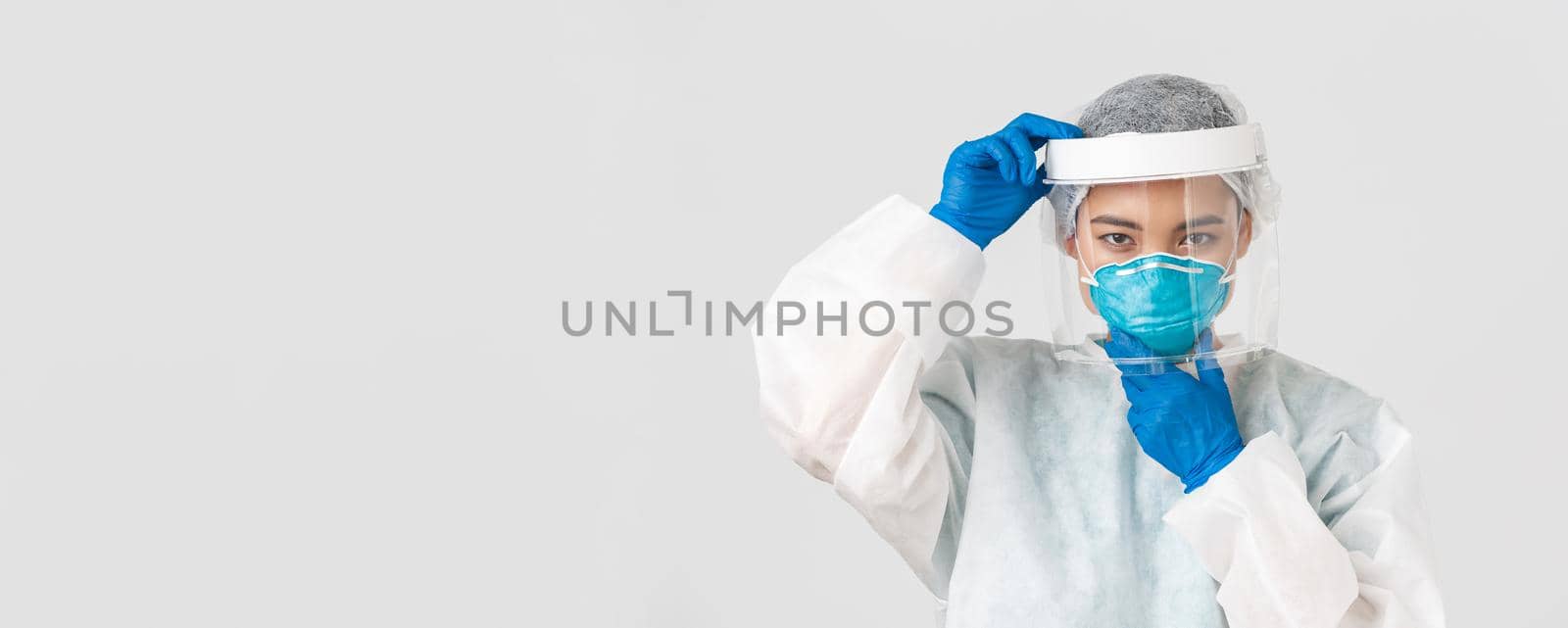 Covid-19, coronavirus disease, healthcare workers concept. Confident serious-looking female asian doctor, put on face shield and respirator, personal protective equipment, white background by Benzoix