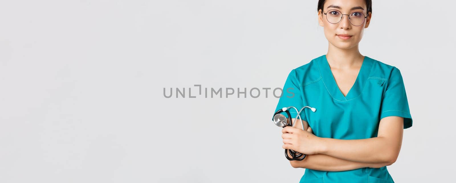 Covid-19, coronavirus disease, healthcare workers concept. Confident smiling professional asian doctor in glasses, cross arms chest, wearing scrubs and holding stethoscope, white background by Benzoix