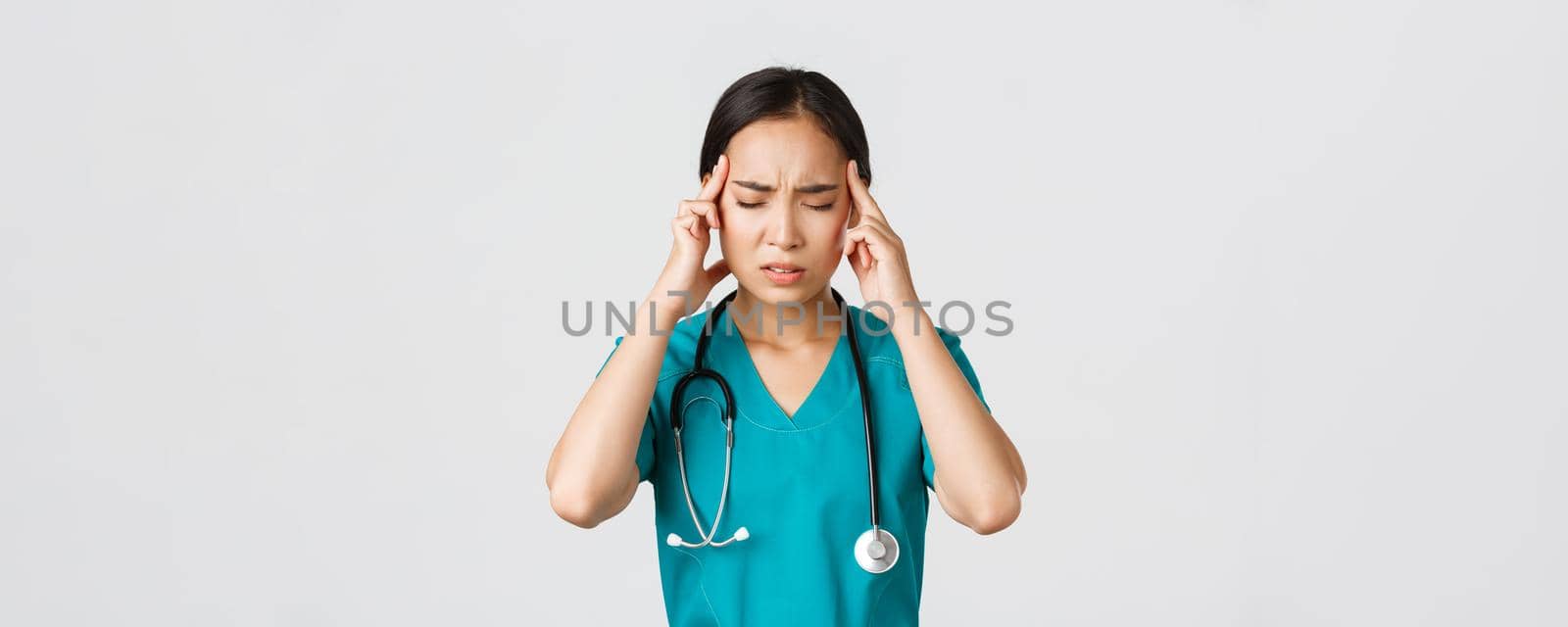 Healthcare workers, preventing virus, quarantine campaign concept. Close-up of overworked and tired asian doctor, nurse having headache, looking troubled, standing white background.