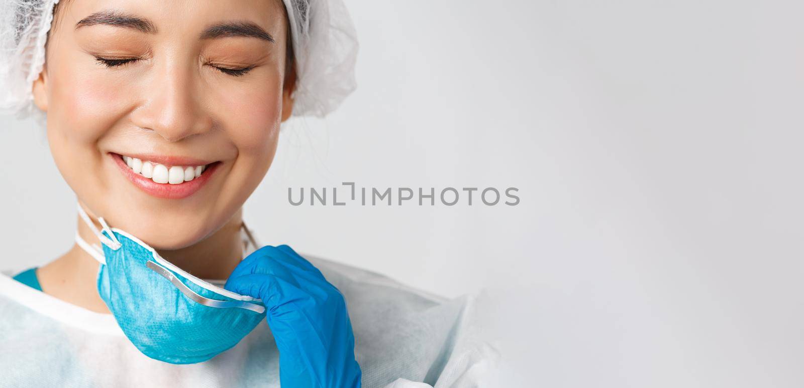 Covid-19, coronavirus disease, healthcare workers concept. Smiling relieved asian female doctor take-off respirator and have skin damage from personal protective equipment, white background.