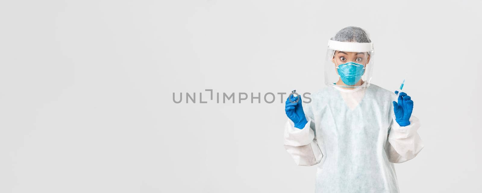 Covid-19, coronavirus disease, healthcare workers concept. Amazed and excited female asian doctor, infectionist in personal protective equipment, holding syringe and ampoule with vaccine.