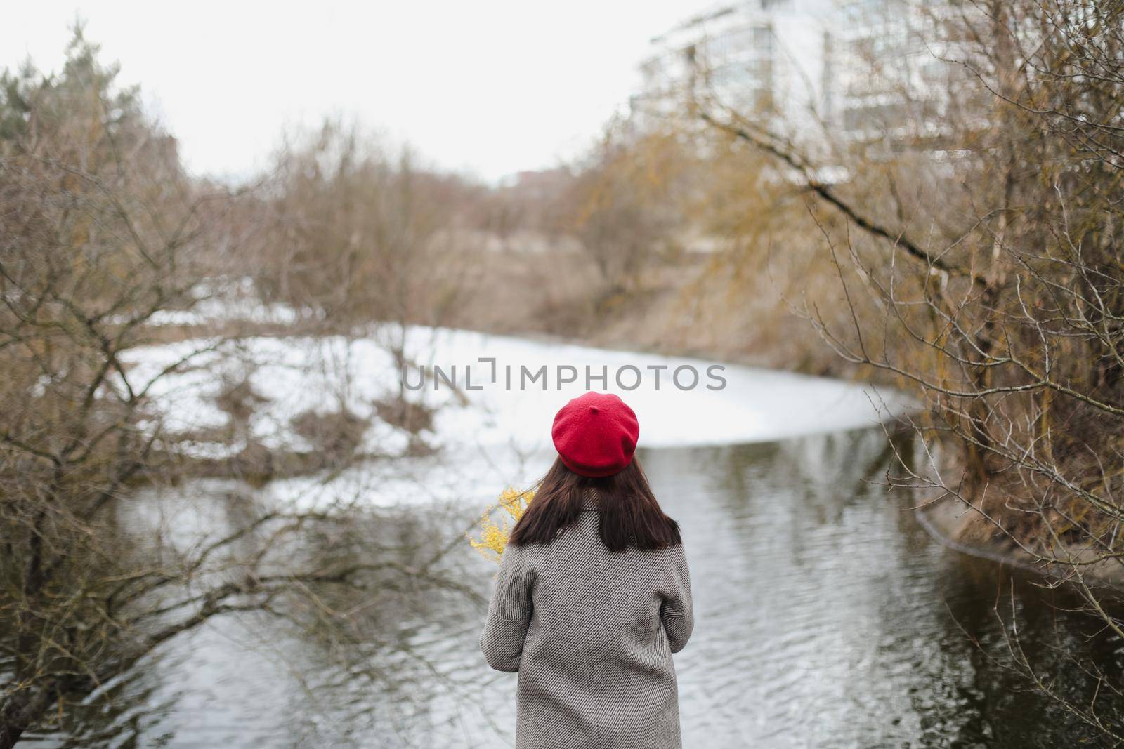 Woman wearing a red hat photographed from behind while looking on the frozen winter lake outdoors