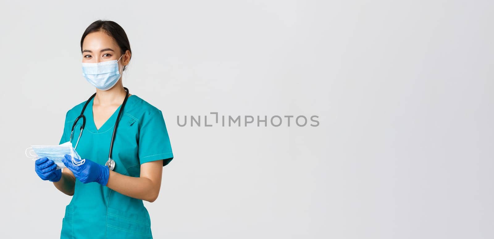 Covid-19, coronavirus disease, healthcare workers concept. Smiling friendly female nurse, physician in scrubs and rubber gloves provide patients with medical masks, white background by Benzoix