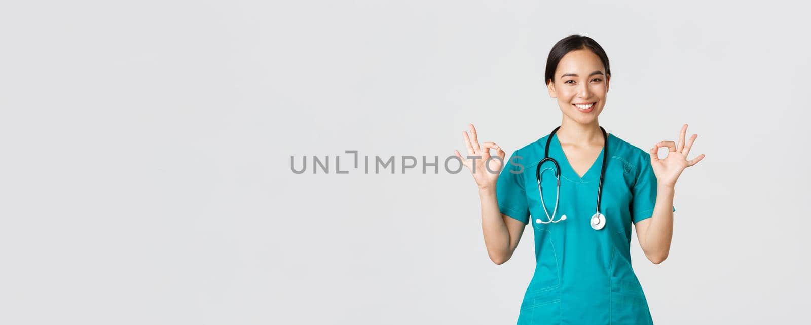 Covid-19, healthcare workers, pandemic concept. Professional confident asian female doctor, intern in scrubs assure patients everything good, showing okay gesture satisfied, smiling pleased by Benzoix