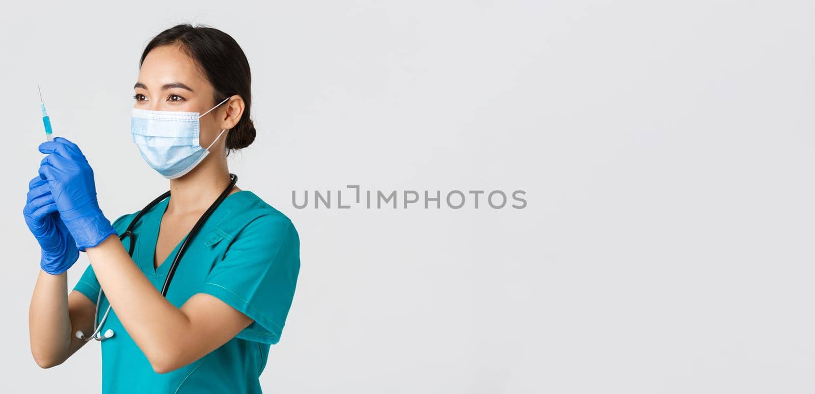 Covid-19, coronavirus disease, healthcare workers concept. Side view of confident smiling asian female physician, nurse prepare syringe with vaccine for flu shot, standing white background.