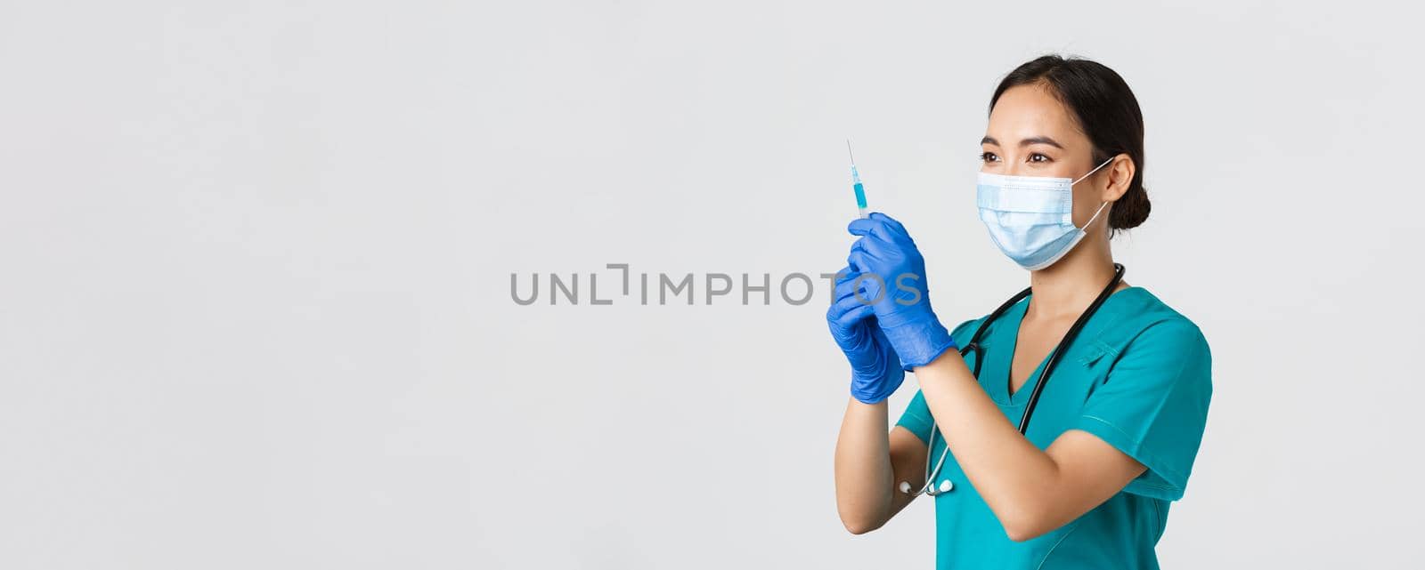 Covid-19, coronavirus disease, healthcare workers concept. Side view of confident smiling asian female physician, nurse prepare syringe with vaccine for flu shot, standing white background.