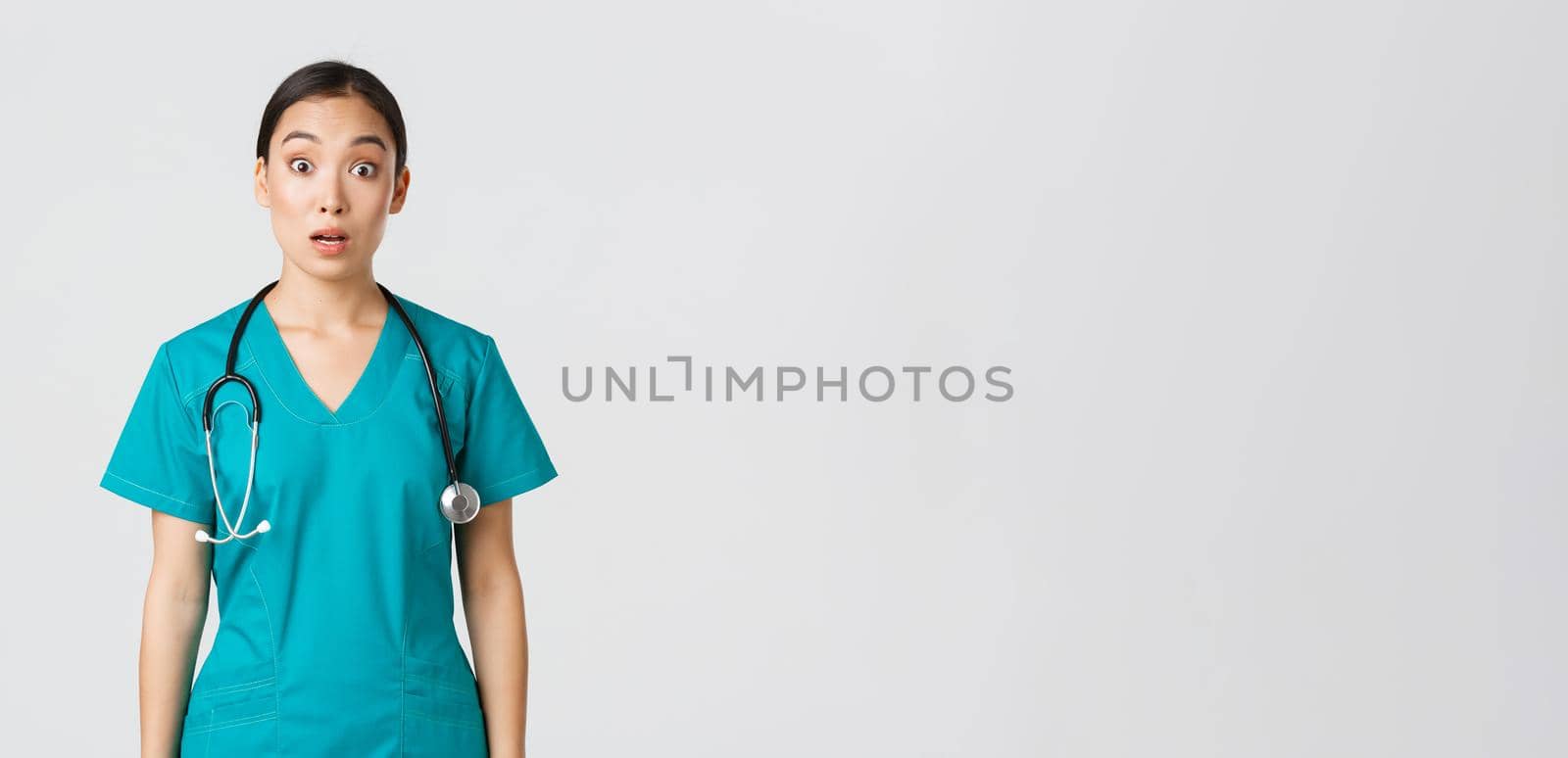 Covid-19, healthcare workers, pandemic concept. Impressed and surprised asian nurse in scrubs drop jaw and stare at camera speechless, looking amazed over white background by Benzoix