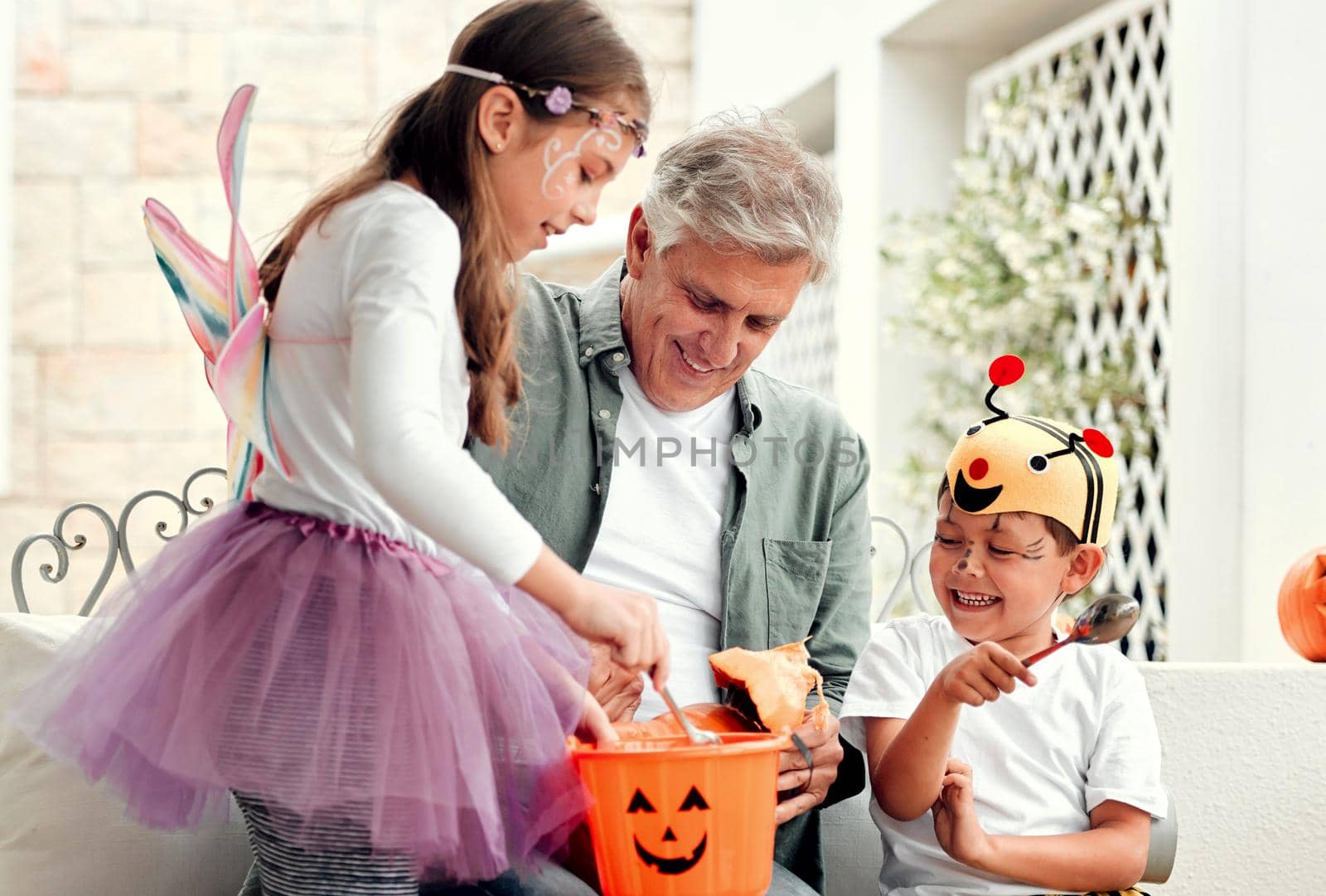 We all love halloween. Shot of two adorable young siblings carving out pumpkins for Halloween with their grandfather at home. by YuriArcurs
