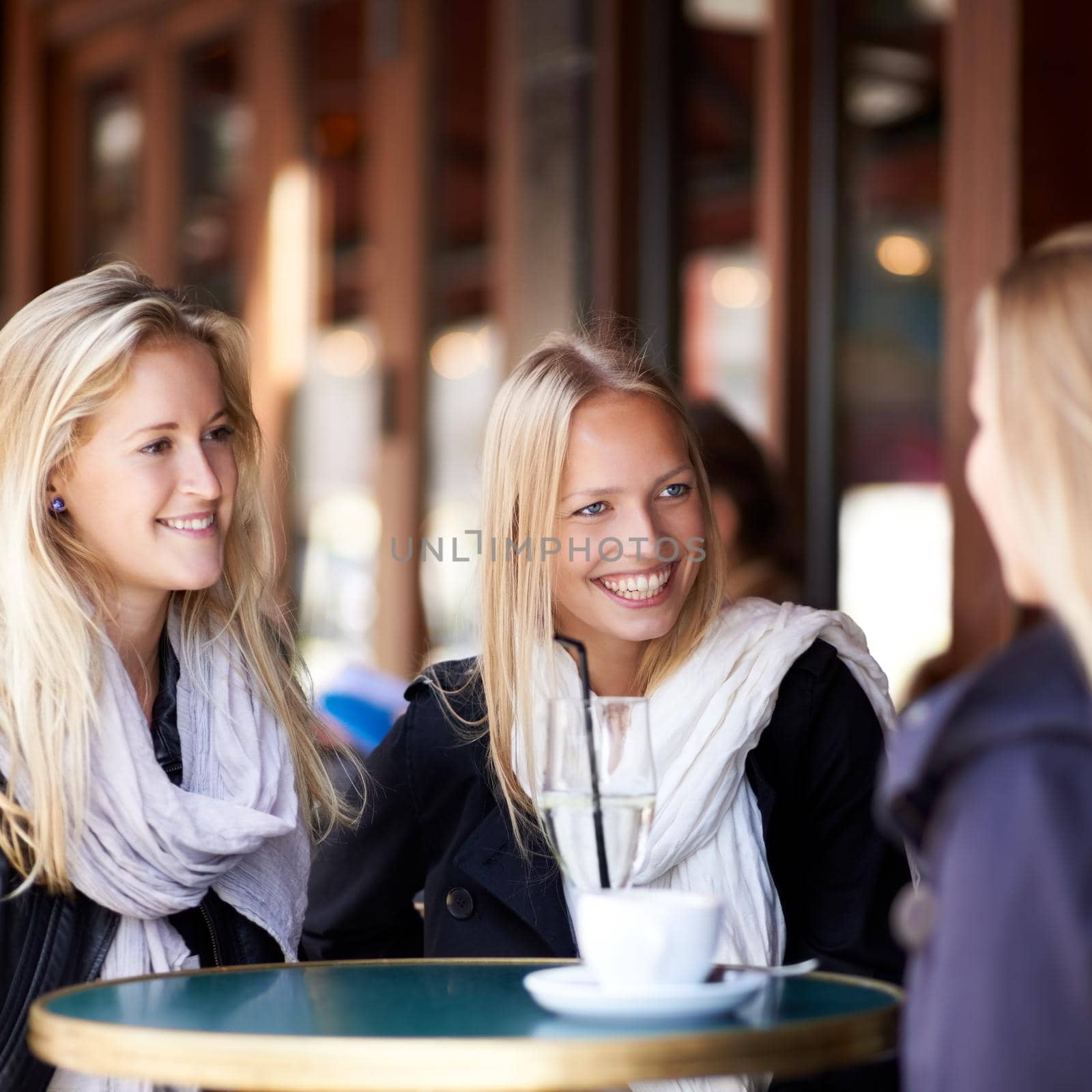 Three friends seated at a coffee shop talking to each other and smiling.