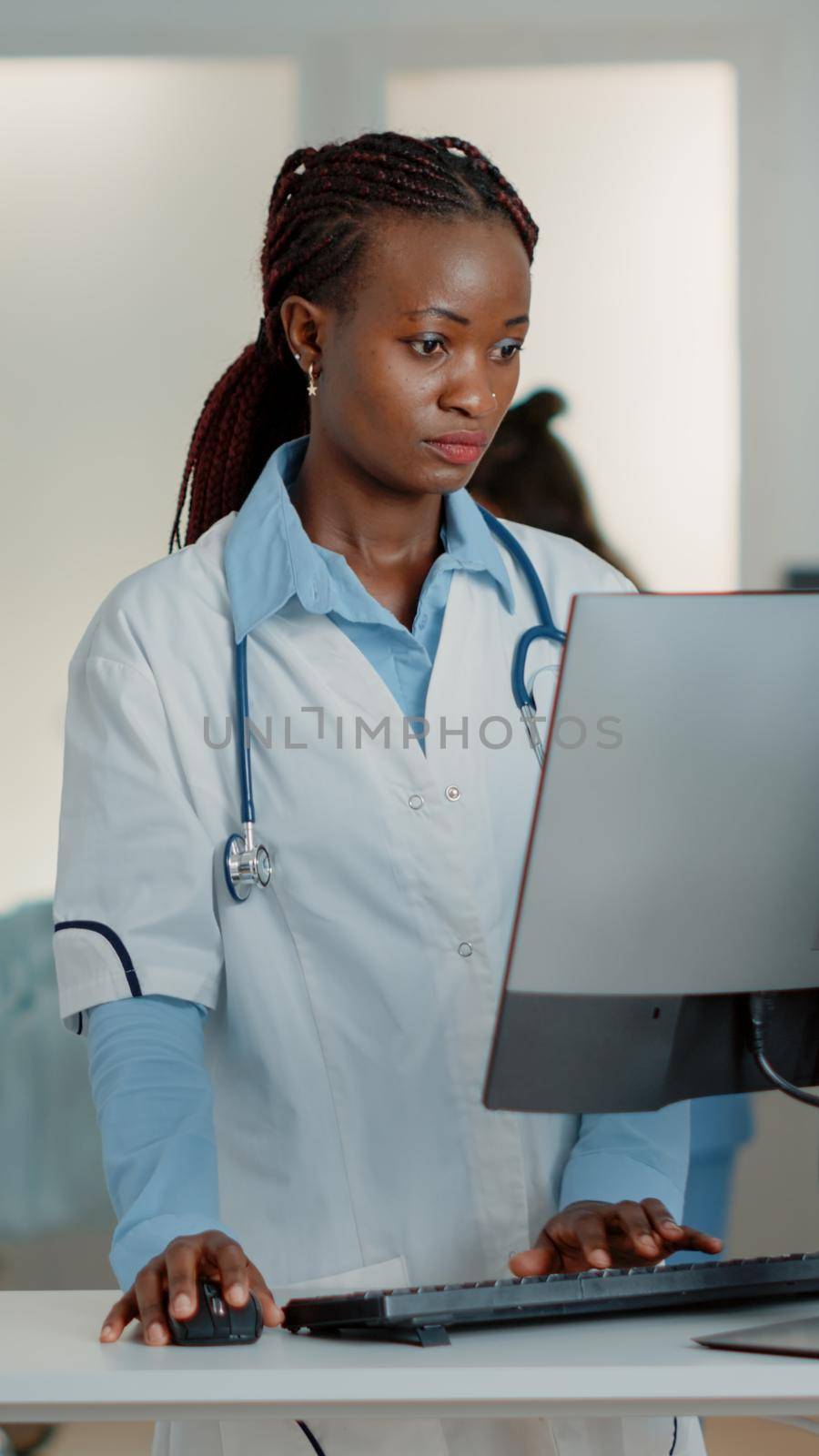 General practitioner with white coat using computer at desk to find medication and treatment against disease. Woman doctor working with technology on monitor to cure sick patient.