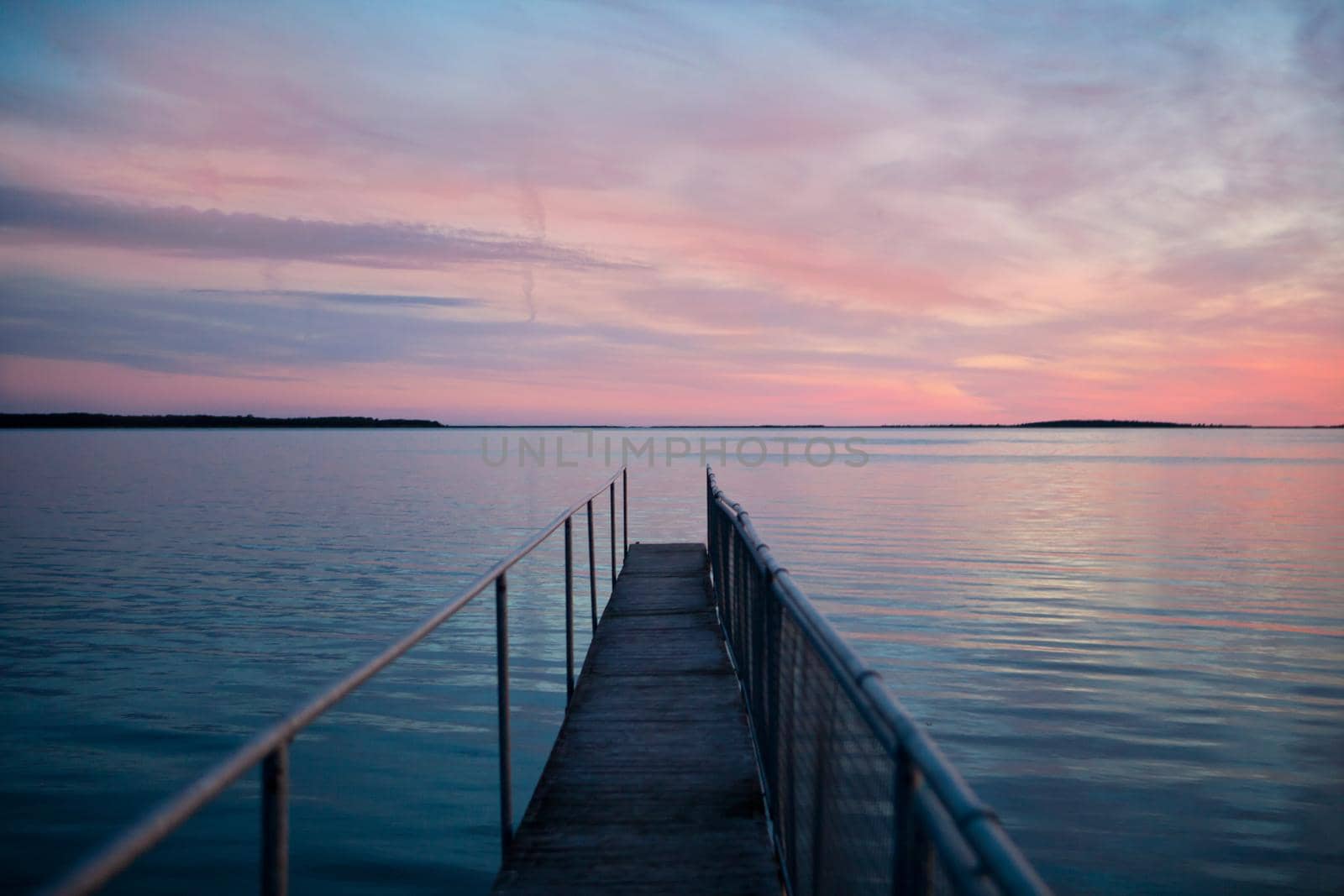 pink sunset at wooden pier on the blue sea. pink sunset at wooden pier on the blue sea. Beautiful view of long jetty. Minimal image with jetty stretching to the ocean. Warm tones of orange, yellow, pink, blue and purple. Smooth water and reflection