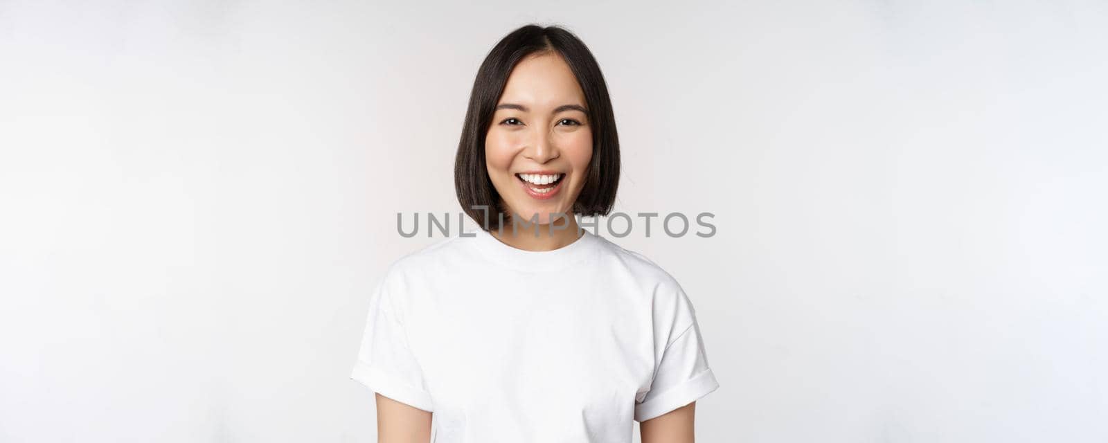 Close up portrait of young asian woman looking at camera, wearing t-shirt, smiling and looking happy, white background by Benzoix