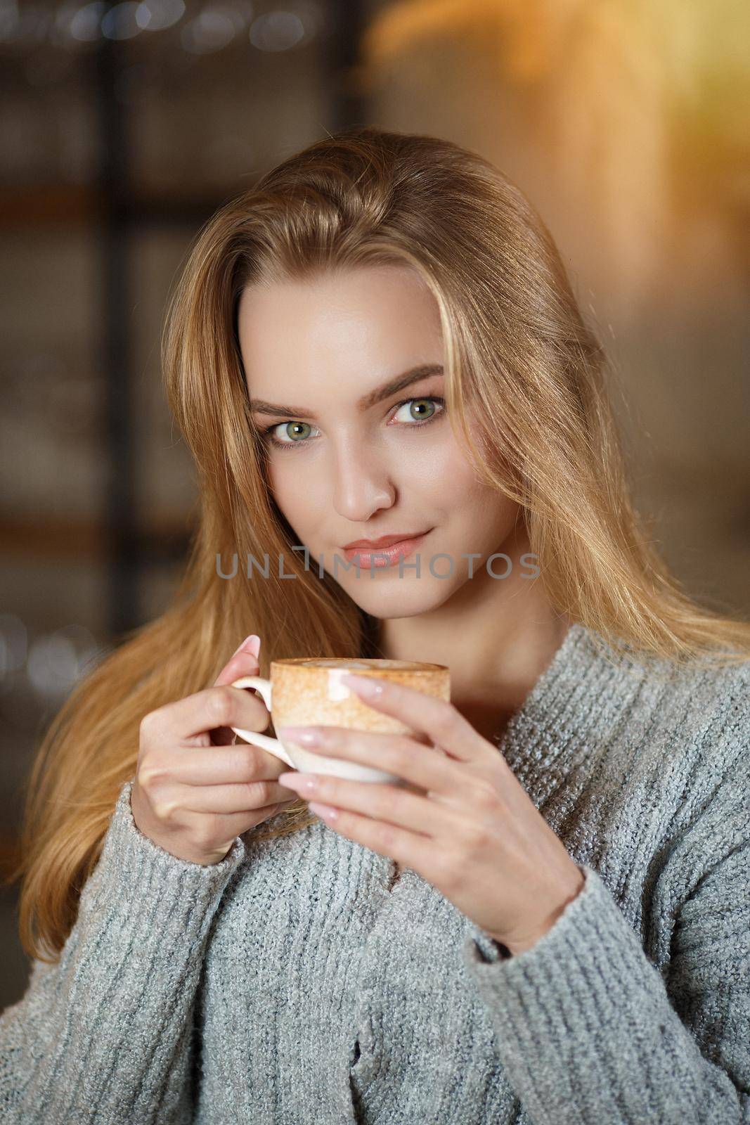 Portrait of a young beautiful woman sitting in modern cafe bar interior having a cup of coffee by Gravika