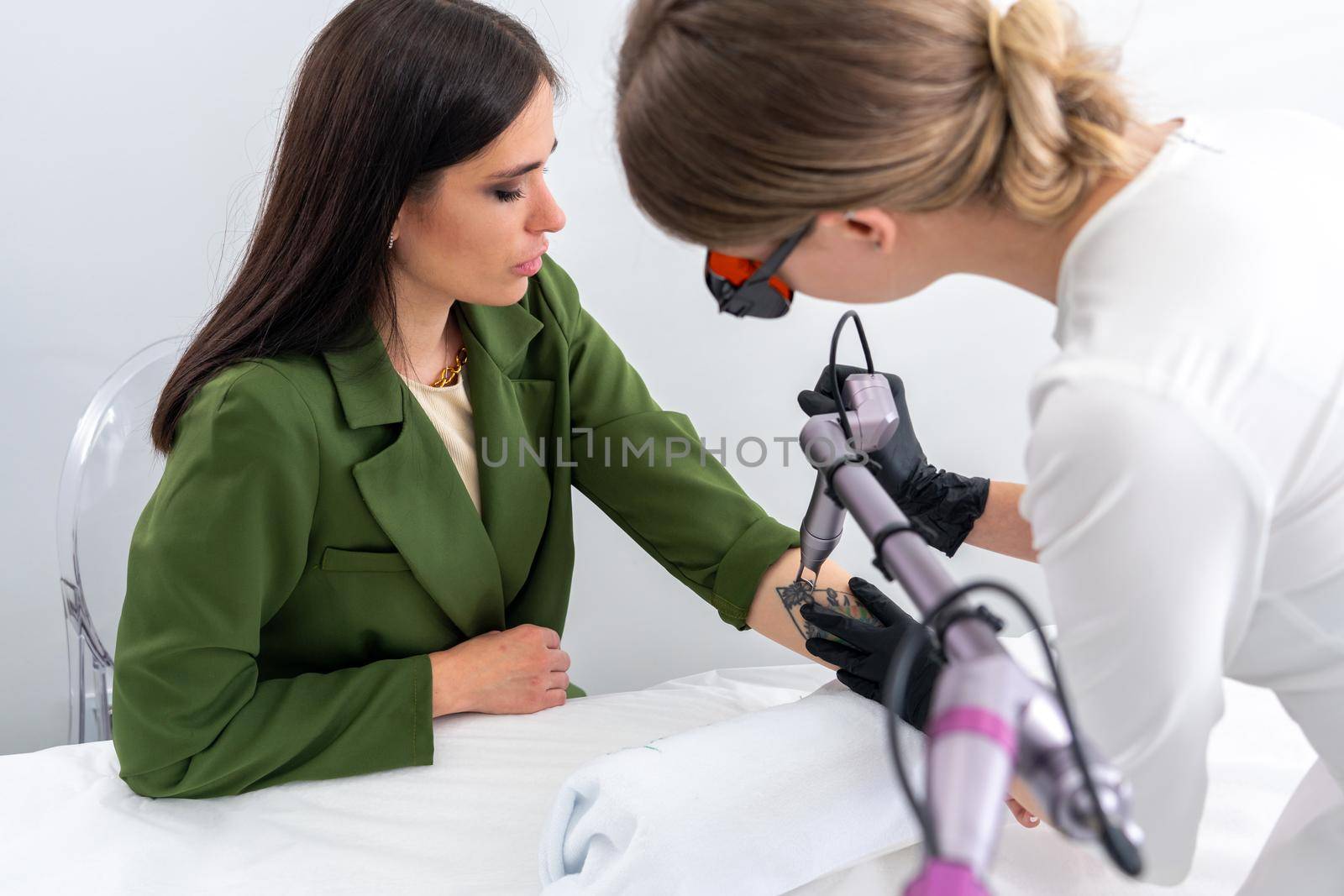 Beautician using laser device to remove an unwanted tattoo from female arm. Concept of erasing tattoos as expensive procedure in cosmetology clinic