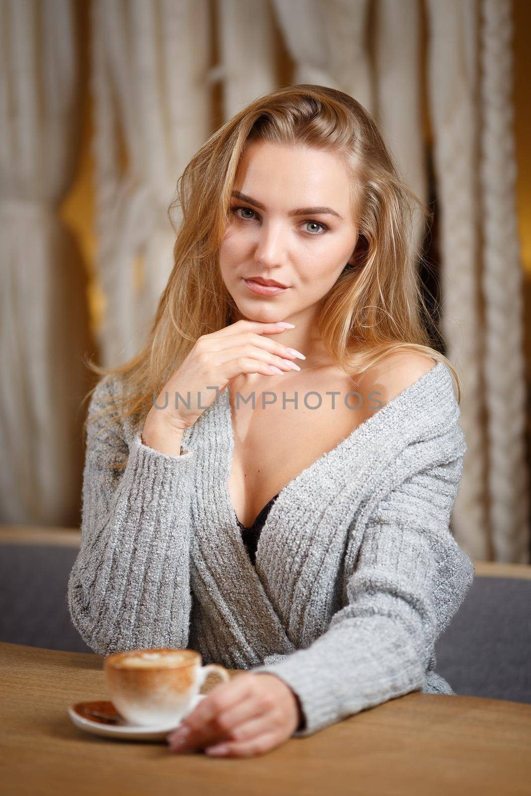 Portrait of a young beautiful woman sitting in modern cafe bar interior having a cup of coffee by Gravika
