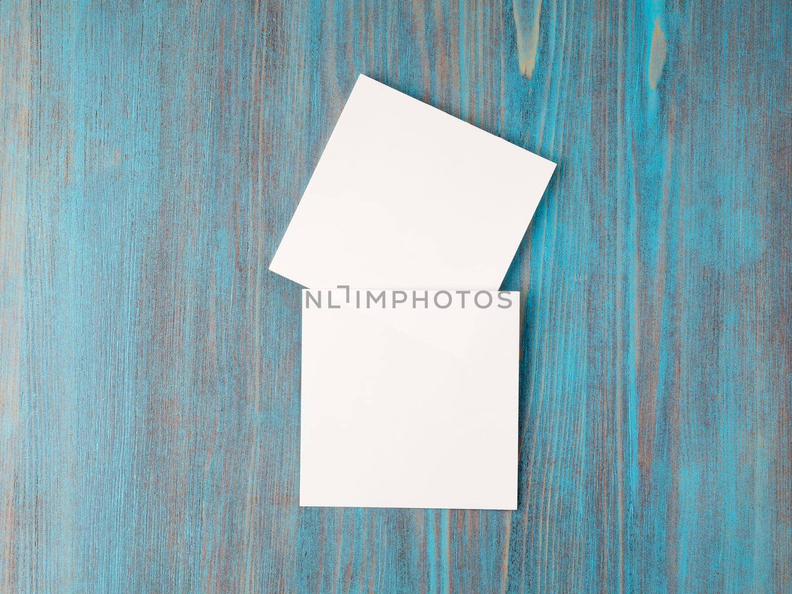 two white piece of paper for notes, square shape for record reminders on a blue wooden table, top view