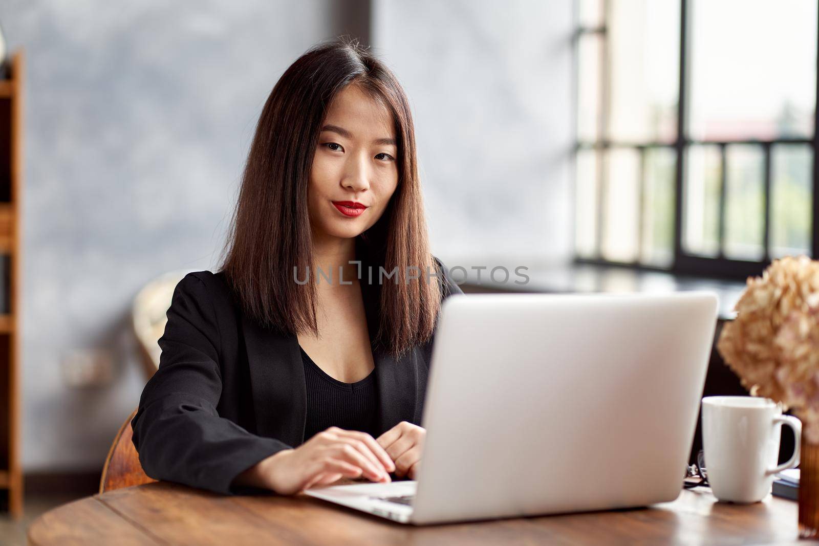 Asian business woman working in laptop in office. Japanese businesswoman work in cafe. Active serious smart female worker looking at camera