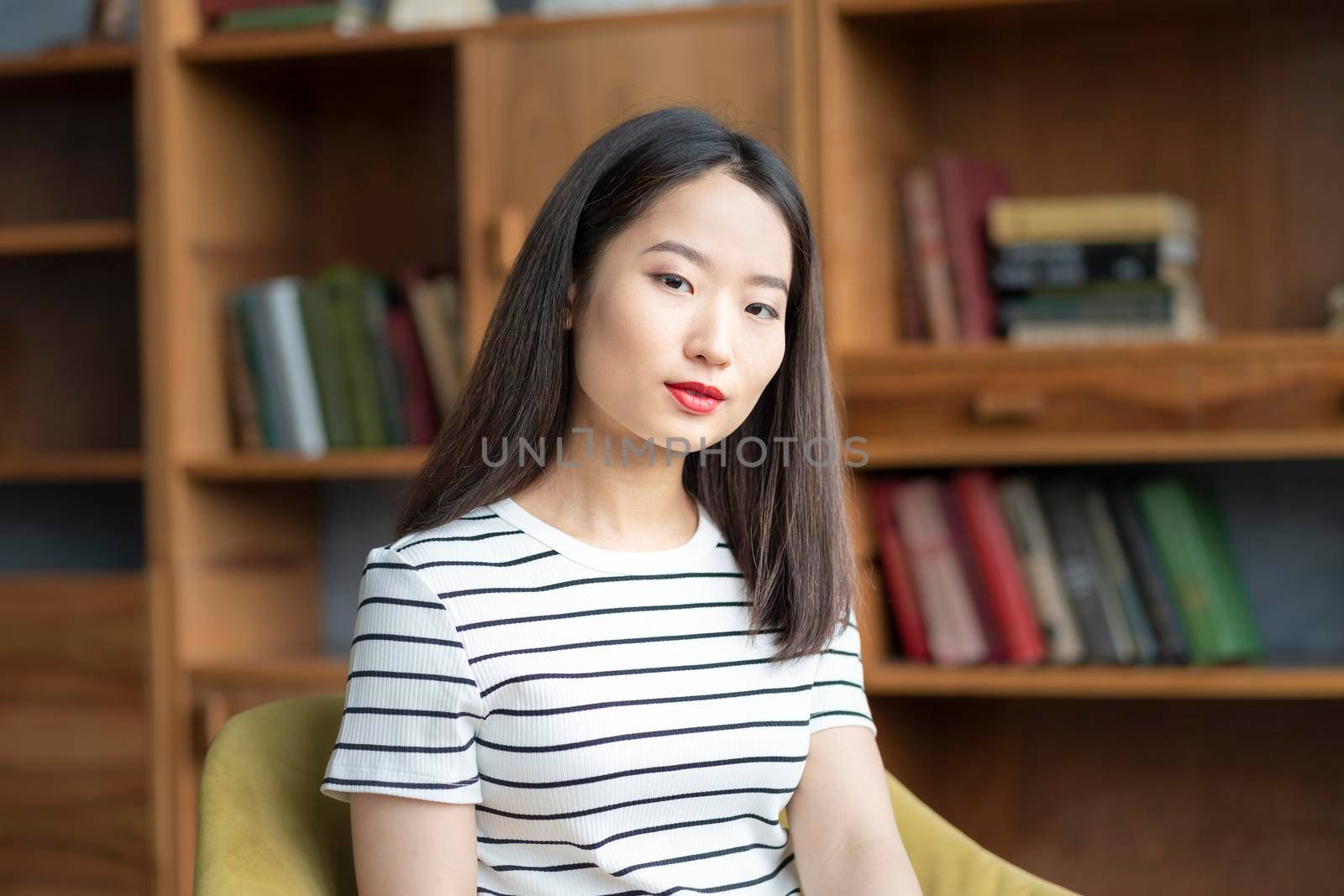 Portrait of beautiful young Asian woman in striped t shirt sitting in chair by NataBene