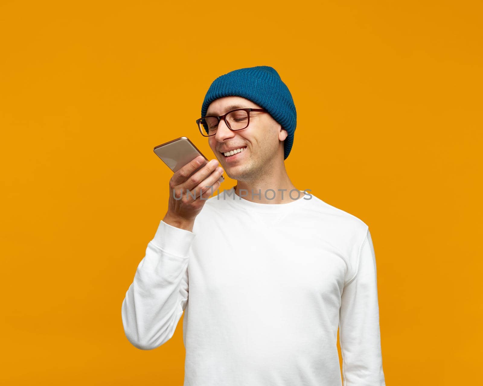 Portrait of positive young man recording audio message, speaking to microphone of mobile phone by NataBene