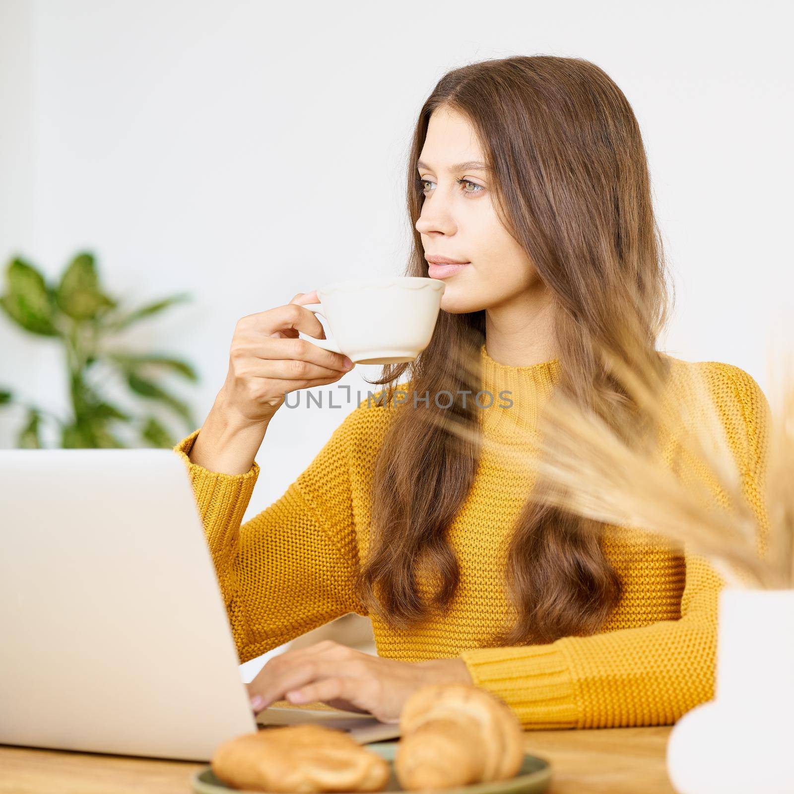 Young female enjoying morning coffee and checking emails on laptop, cafe interior. by NataBene