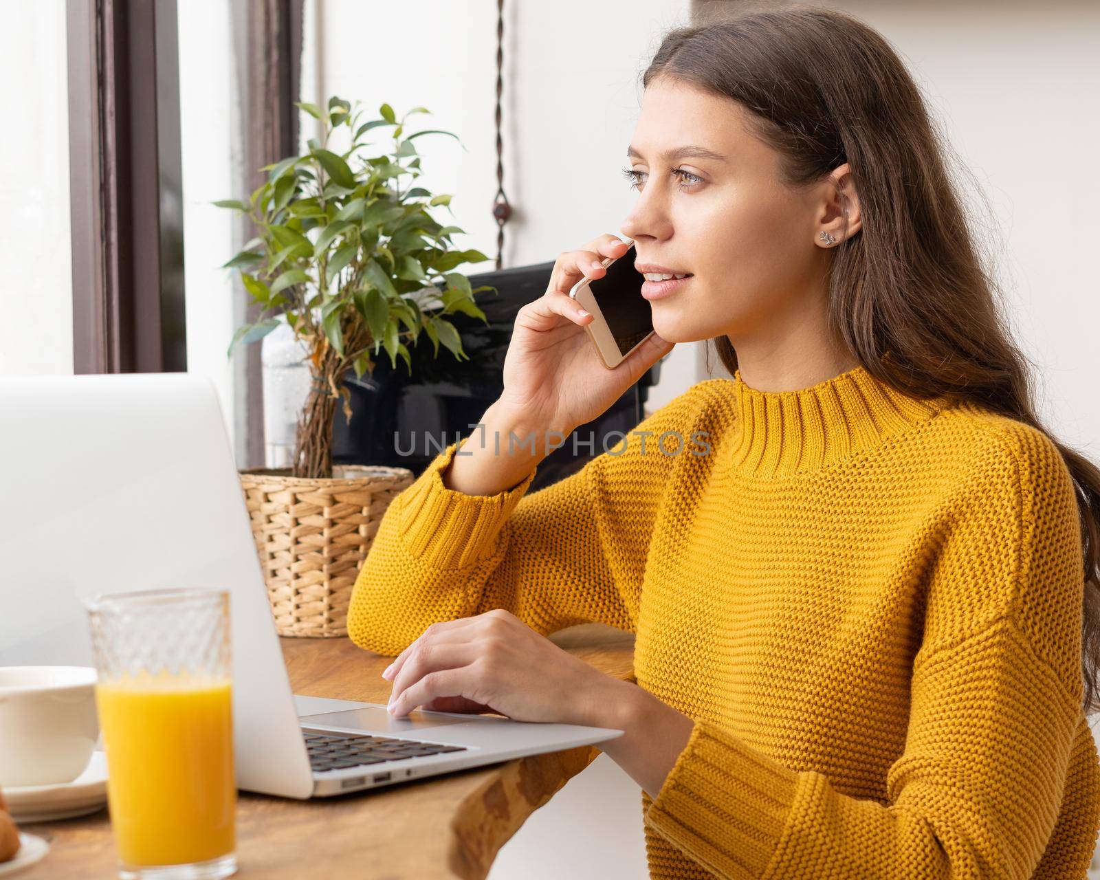 Digital nomad. Young female entrepreneur talking on mobile phone, looking at laptop and smiling, happy woman working in cafe or from home.