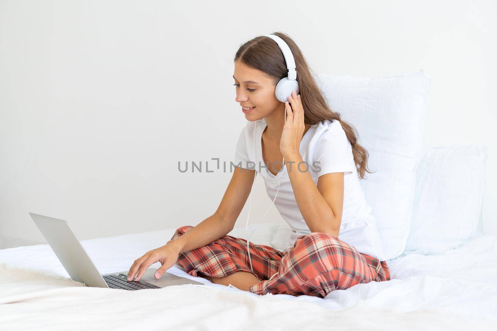 Young female in headphones studying online, working from home using laptop, hotel interior, copy space. Gig economy, digital nomad,