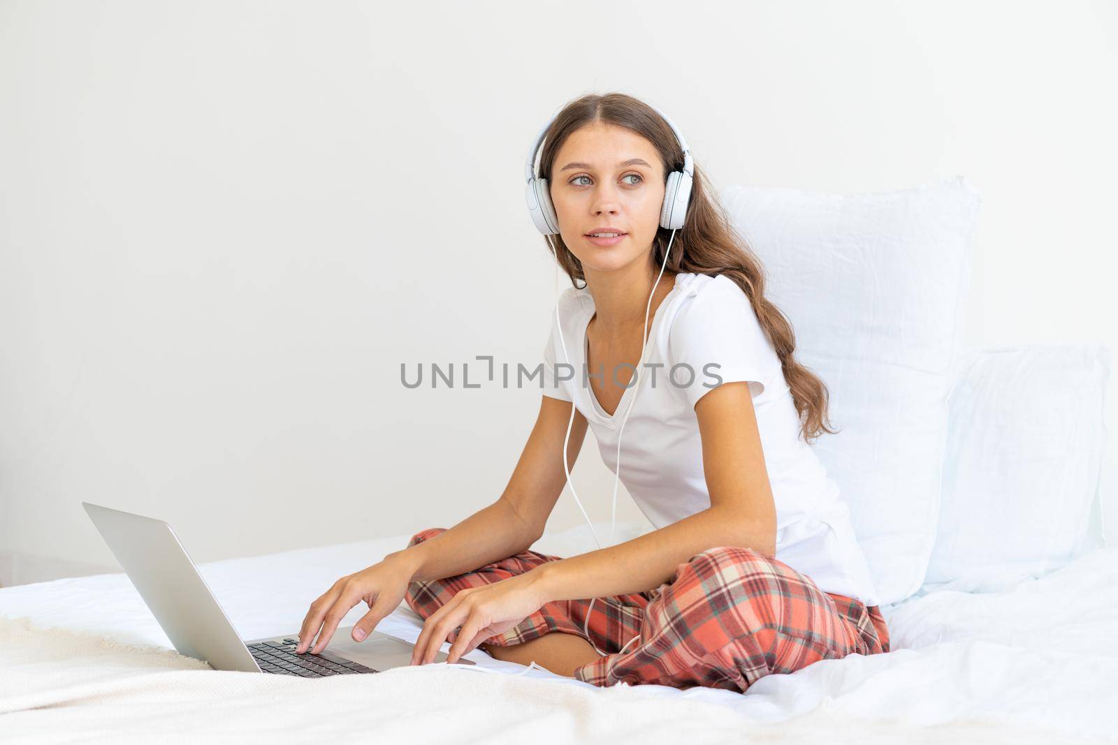 Young woman in headphones studying online, working from home using laptop by NataBene