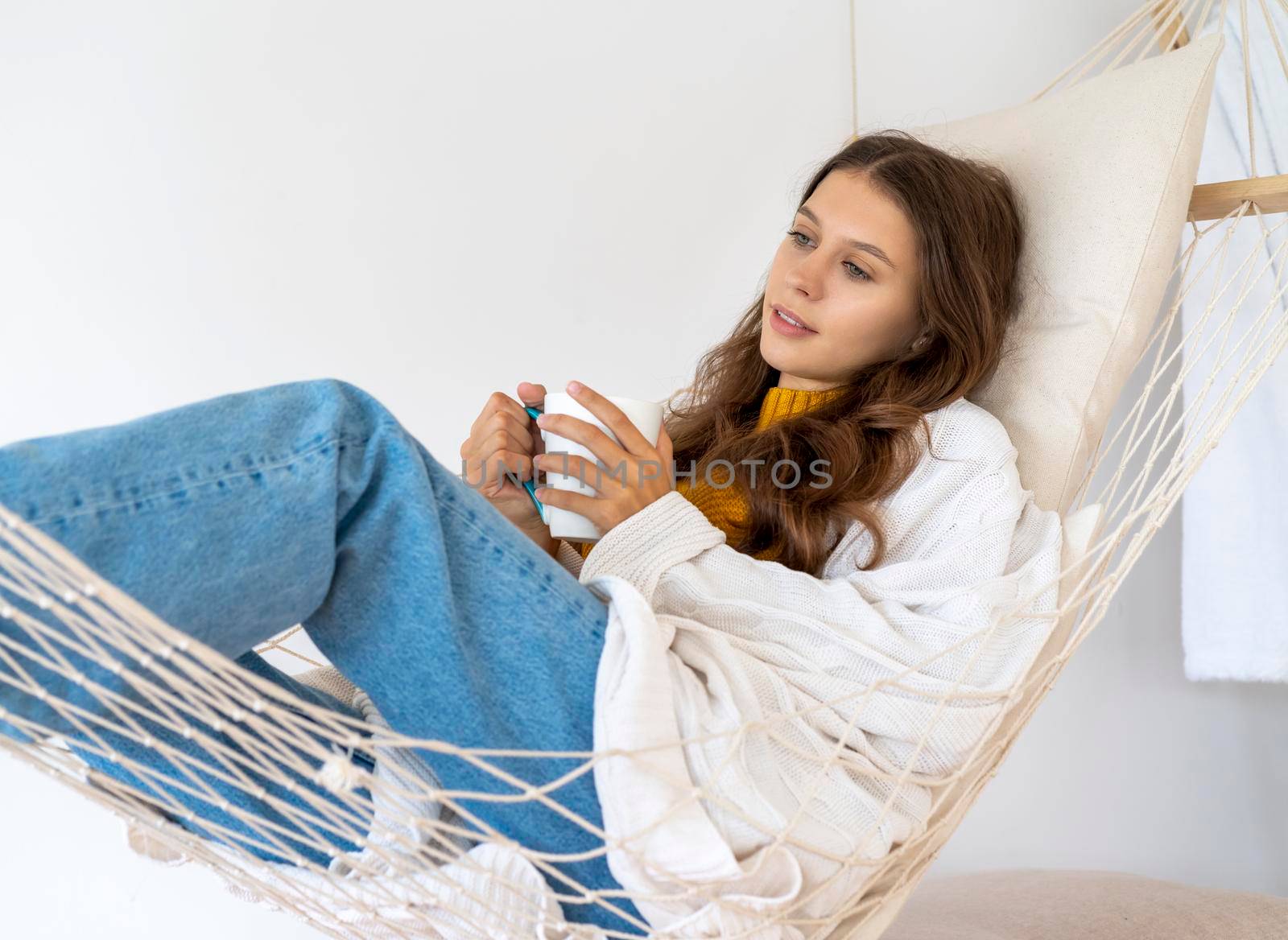 Cup of tea or coffee. Woman drinking hot beverage and enjoying morning, sitting on hammock and dreaming, relaxed mood.