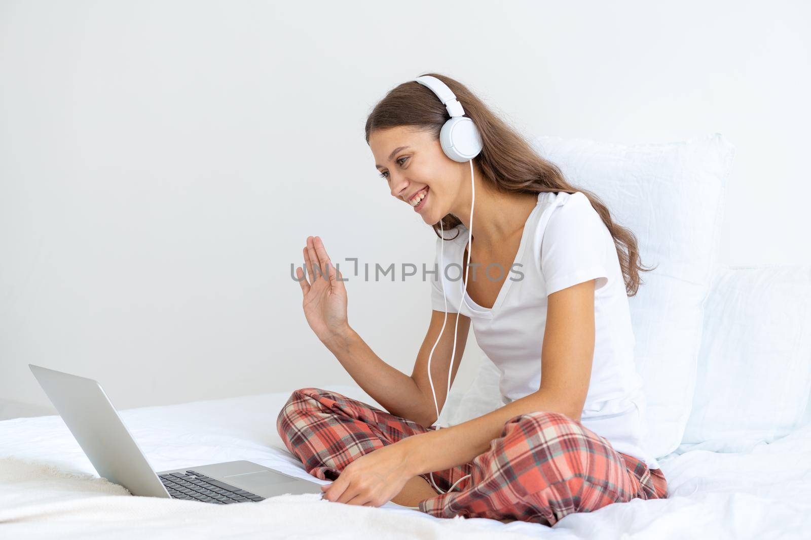 Young girl with headphones talking on conference calls, waving hand, smiling. by NataBene