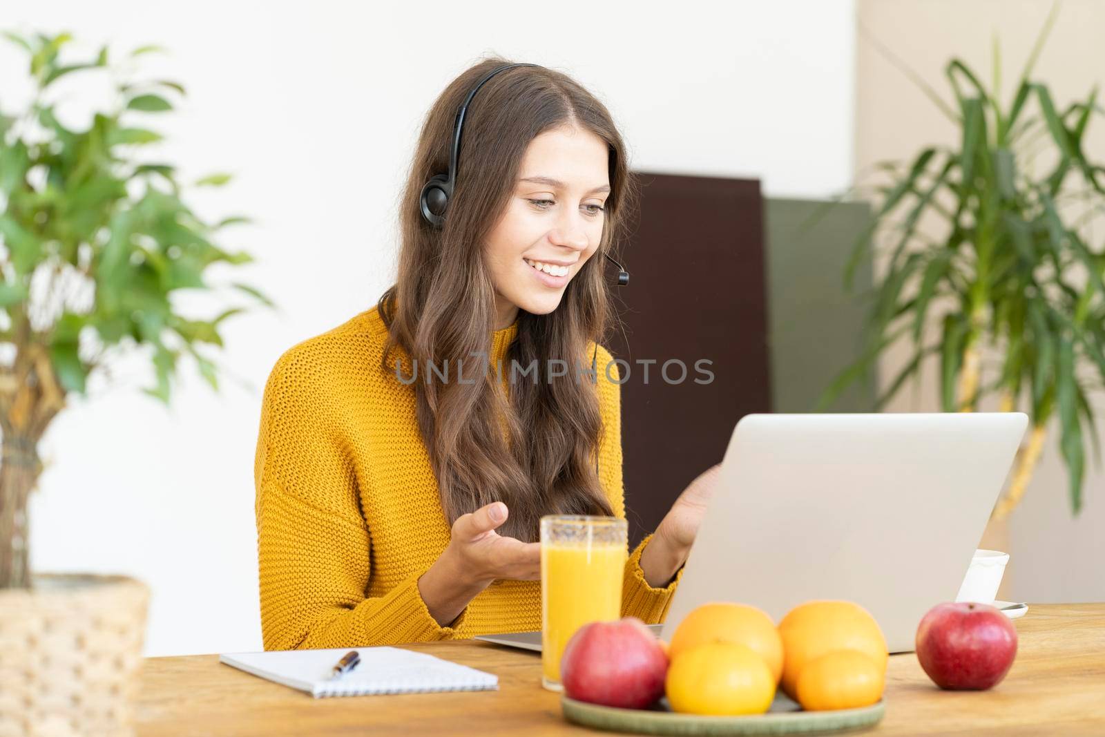 Happy woman in headset speaking by conference call and video chat on laptop in office. Online education, course. Support service agent consulting customer.