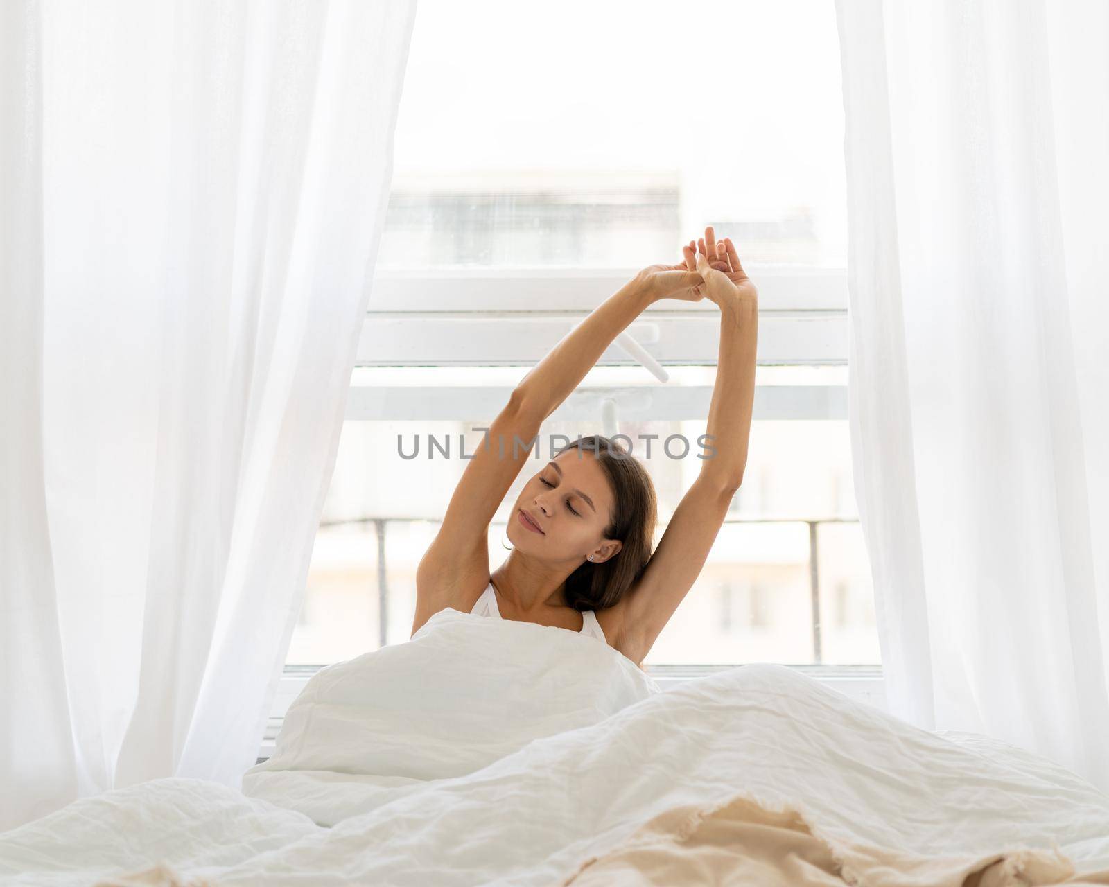 Young woman stretching in bed after wake up, entering new day happy by NataBene