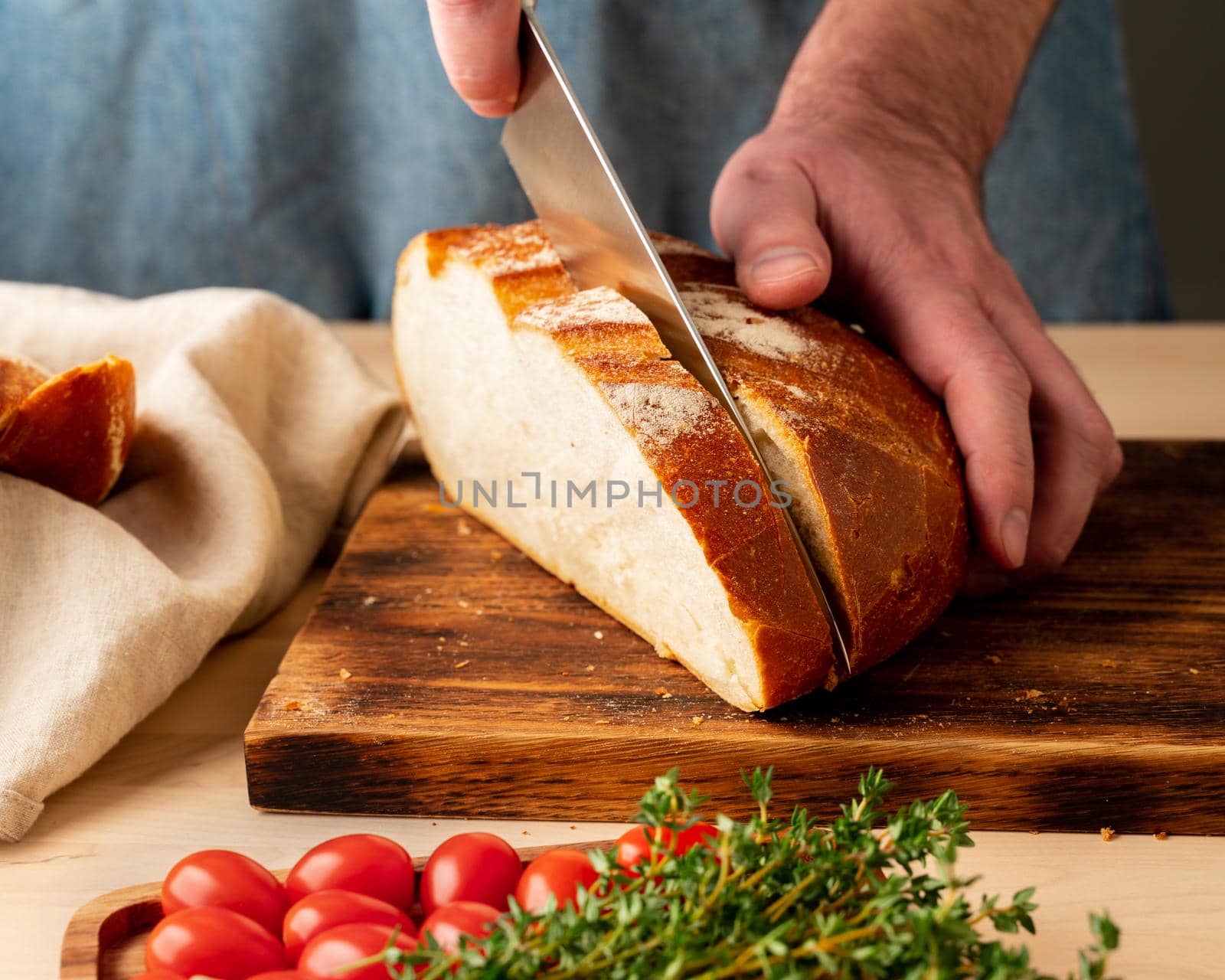 Faceless man cutting fresh home-baked crusty bread with large knife by NataBene