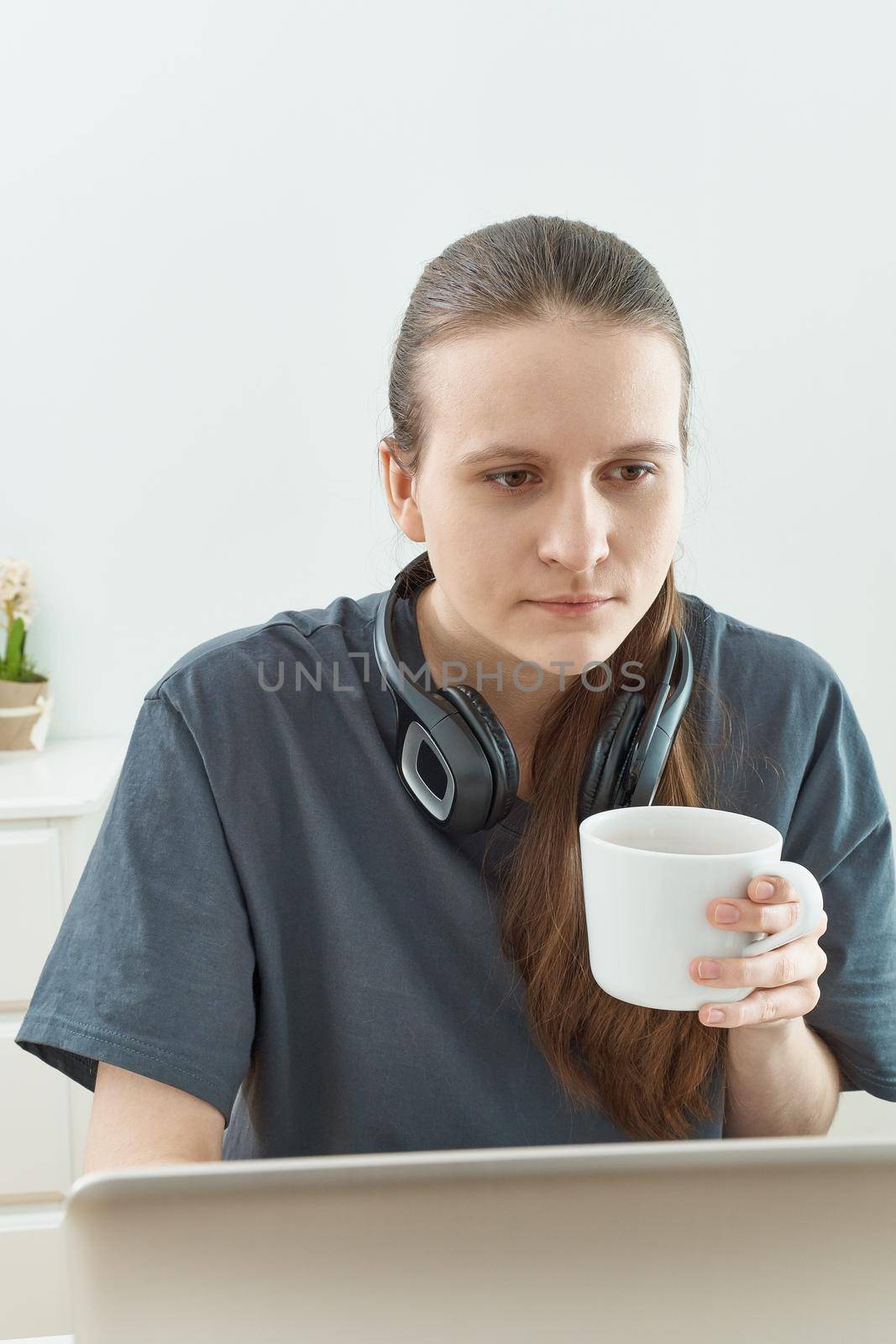 Girl with headphones playing tired of playing games on computer on computer, woman has taken a break and is drinking tea. Quarantine, self-isolation, sociophobia.
