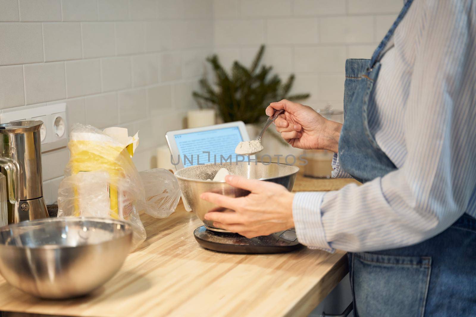 Faceless woman cooking and baking dough on kitchen table at home, apartment, flour, scales, bowls, digital tablet with recipes on table. Homemade food