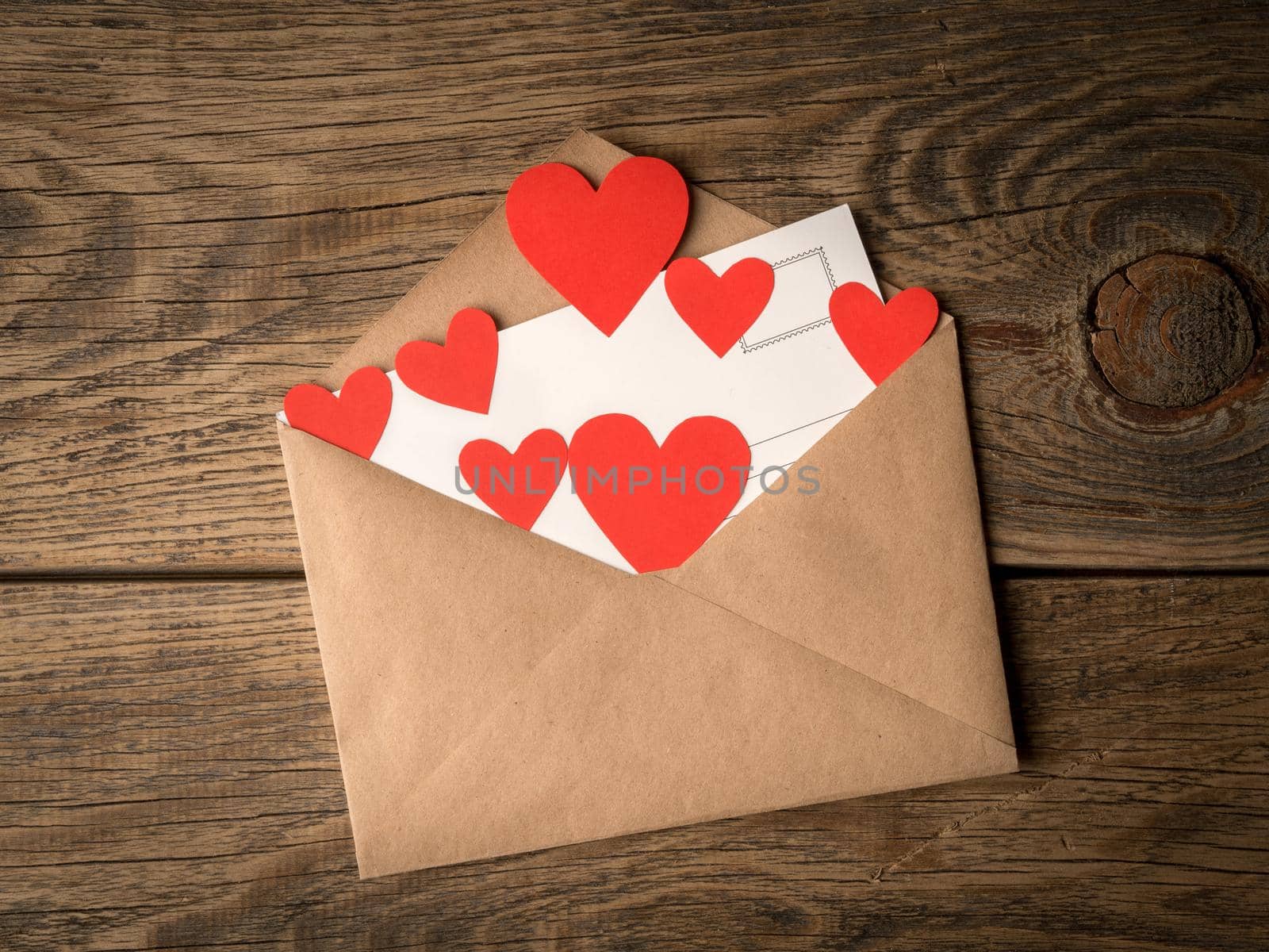 card and red hearts in open envelope from brown Kraft paper on wooden aged vintage background. Greetings with Valentine's day
