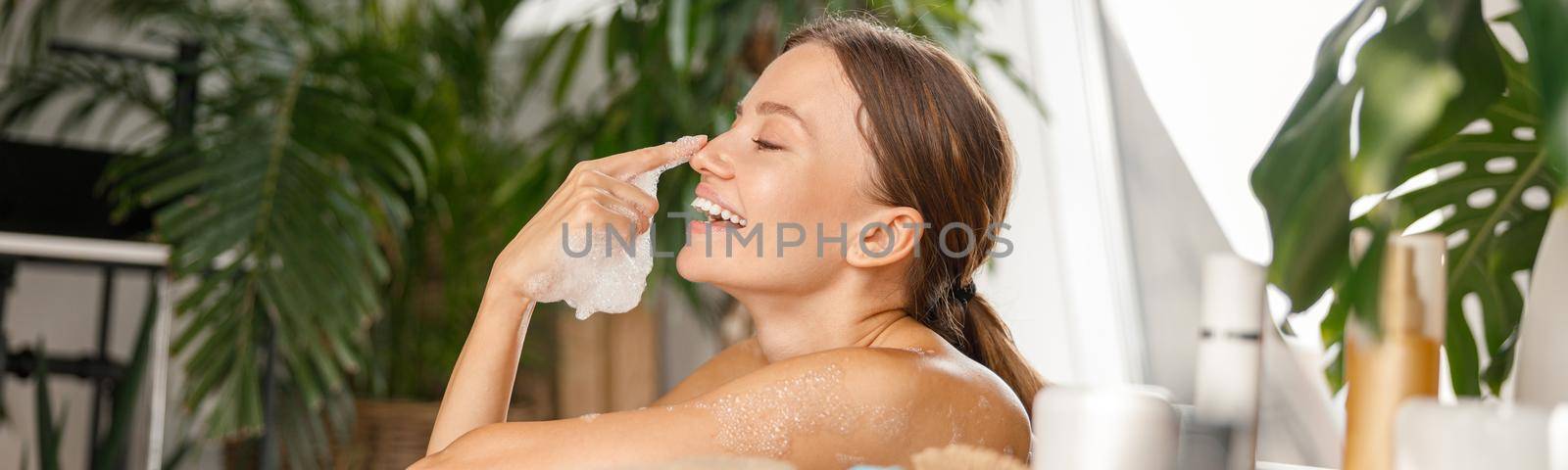 Cute young woman having fun, playing with soap bubbles while bathing at tropical spa resort by Yaroslav_astakhov