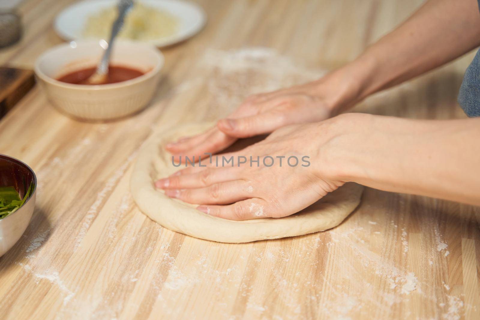 Faceless woman kneading dough on kitchen table at home, apartment, flour, scales, bowls, digital tablet with recipes on table. Homemade food