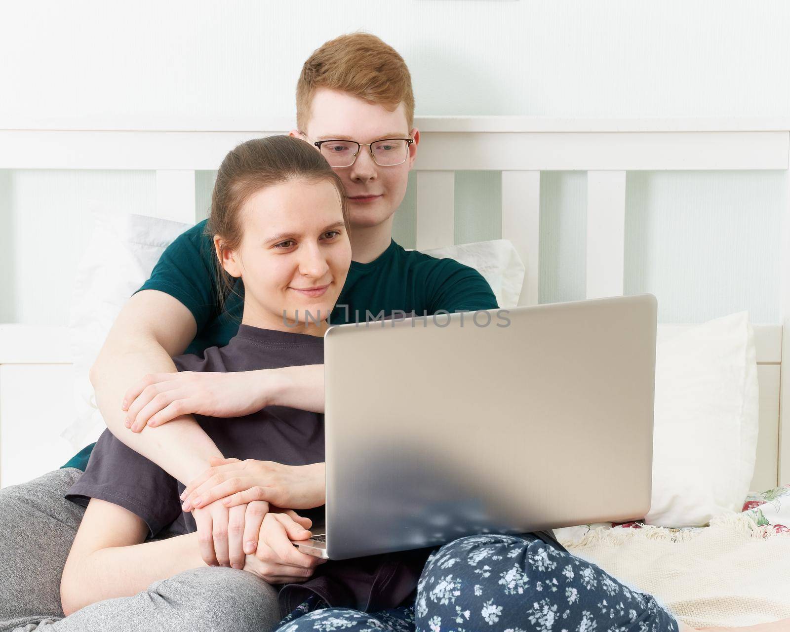 Teen in love lying on bed, watch movies on laptop during quarantine due to coronavirus pandemic. Boy and girl relaxing while staying at home. Concept of self-isolation, sociophobia